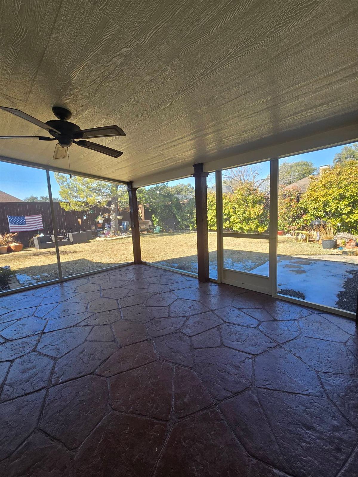 Interior of an enclosed screen room with a ceiling fan overlooking a pool