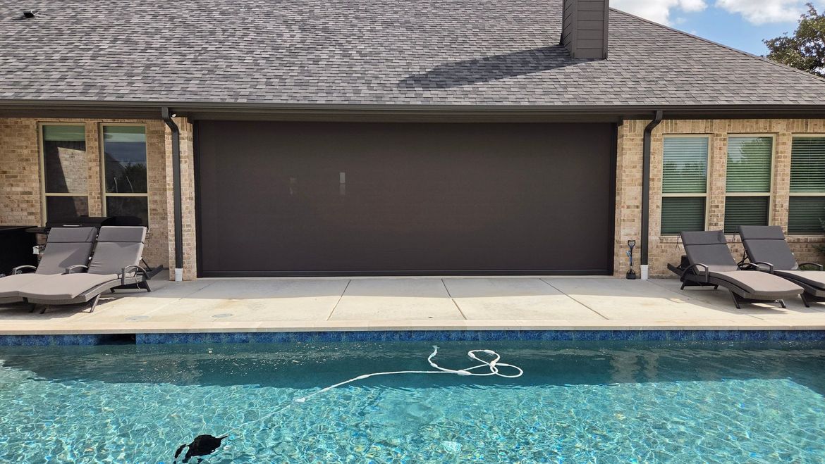 Wide motorized patio screen covering a full garage-width opening beside a DFW pool